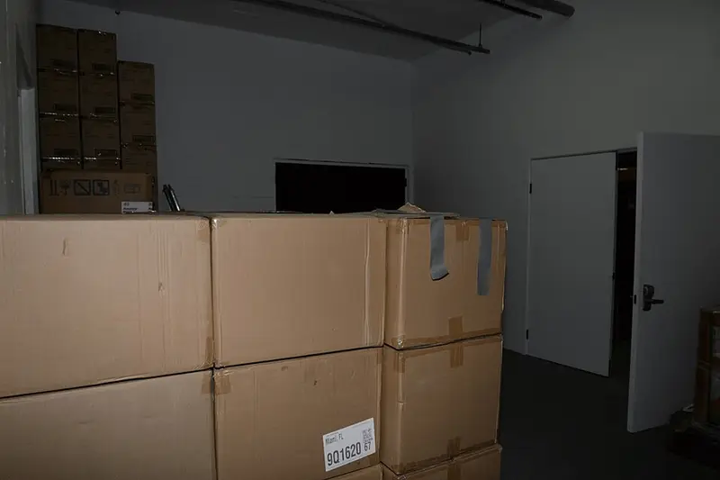 EFTA00002250 - Stacks of cardboard boxes in a dimly lit storage room with a white door open